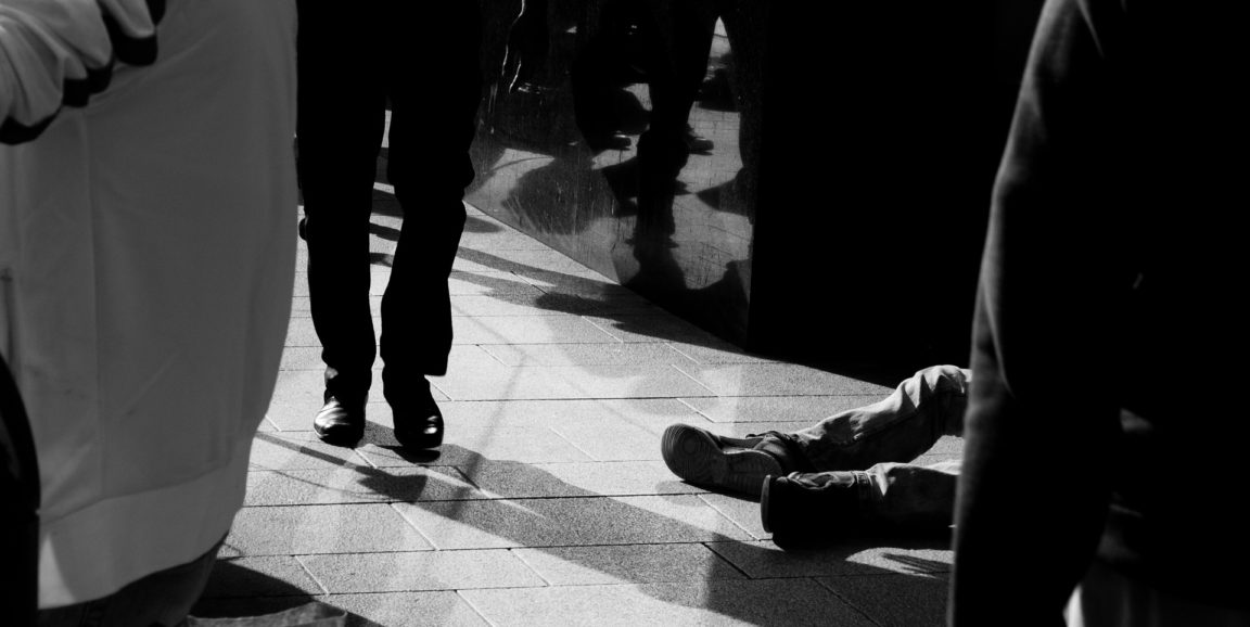 homeless person sitting on ground in crowd of people