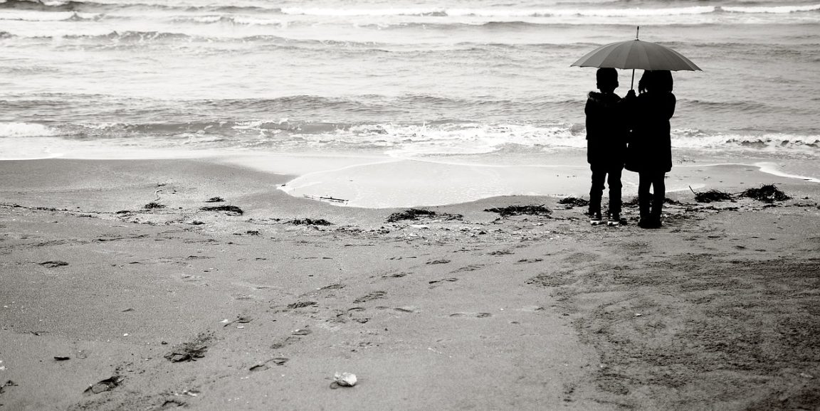 Children standing on a beach sharing an umbrella.