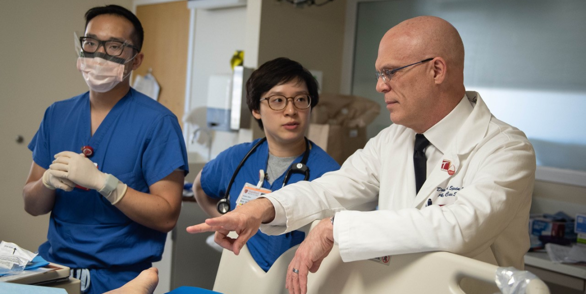 Stanford Chief of Accute Care Surgey David Spain and two clinicians talk with a patient (not pictured) at their bedside.