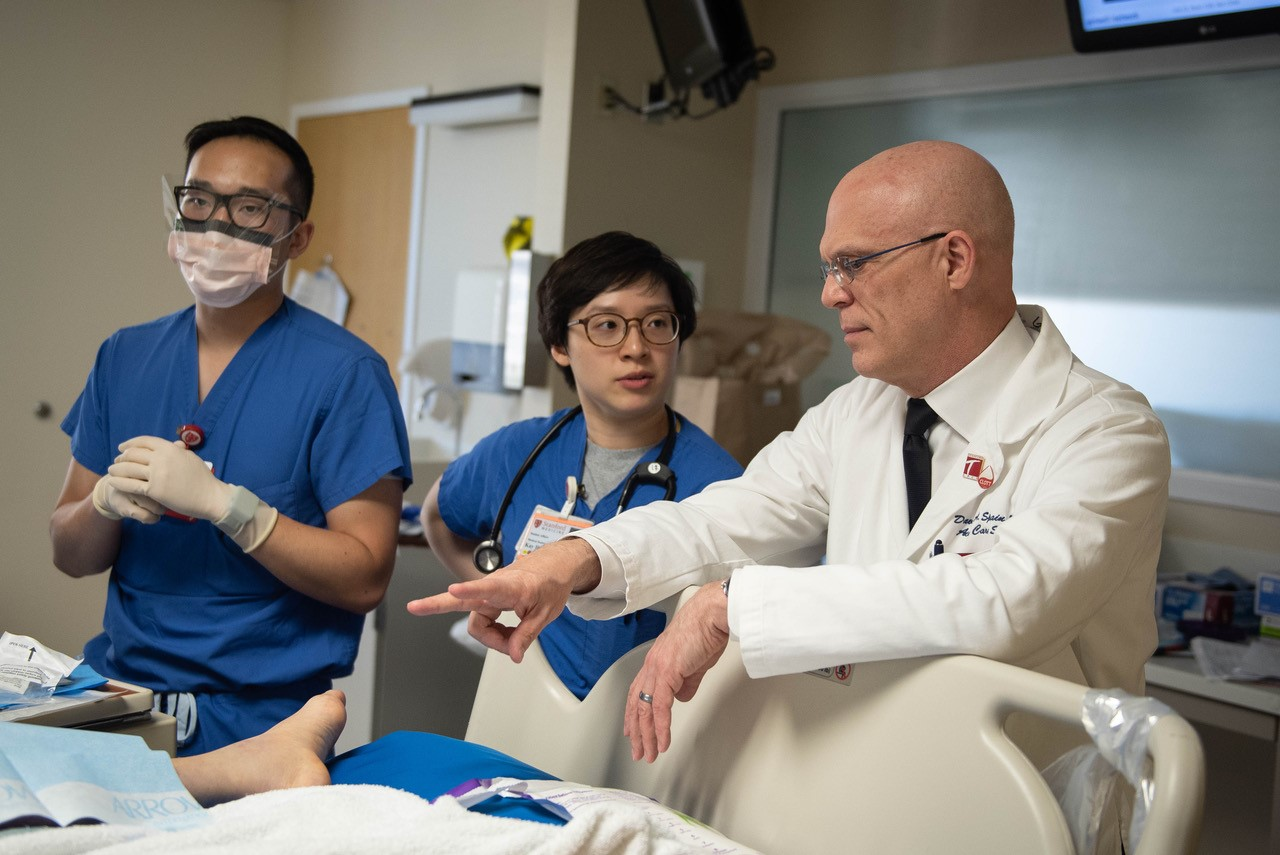 Stanford Chief of Accute Care Surgey David Spain and two clinicians talk with a patient (not pictured) at their bedside.