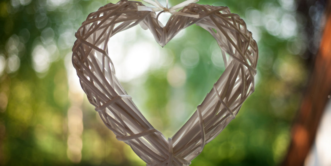 White woven heart ornament against a green sunlit background