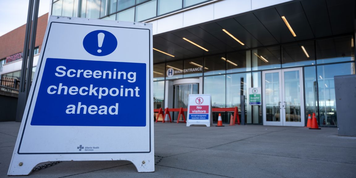 A sign in front of a health center reads "Screening checkpoint ahead"
