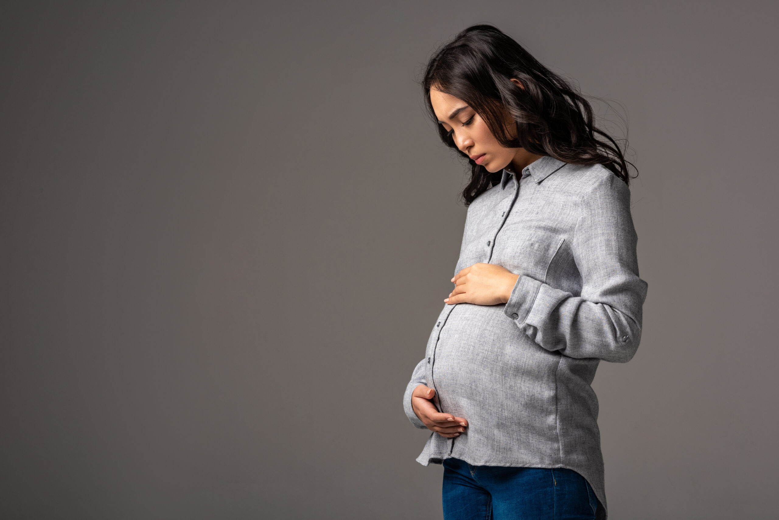 Serious pregnant asian woman in grey shirt and blue jeans looking at ...